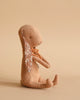 Side view of a Maileg Bunny - Powder sitting upright against a beige background. The toy is made of recycled polyester with a floral pattern on its inner ears and an orange ribbon around its neck. Its limbs are relaxed, and it has a minimalist facial expression.