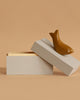 The Ferm Living Hand Carved Wooden Harbour Box - Fish, a beige rectangular box with a partially open lid, sits on a tan surface. A bird figurine made from FSC certified aspen wood rests atop the lid, ideal for kids' room decor against a light brown background.