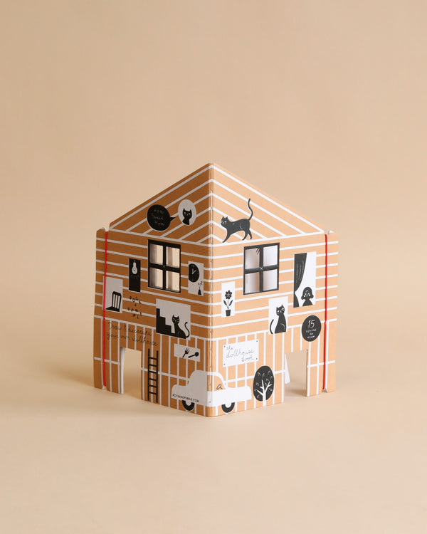 A colorful, illustrated cardboard playhouse featuring designs of windows, a teddy bear, a bicycle, and plants on a beige background called The Dollhouse Drawing Book.