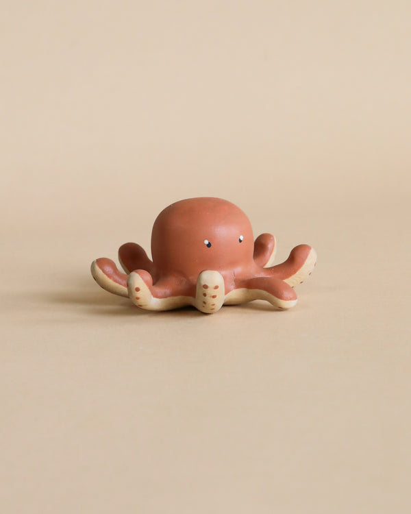 A small, handcrafted wooden sculpture of an octopus, displayed against a plain, beige background. The octopus has a serene expression and its tentacles are spread out symmetrically.