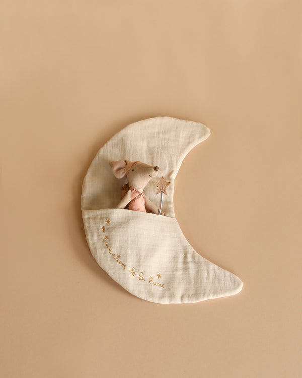 A small, plush mouse in a pink outfit holds a star-shaped wand and rests inside a tooth fairy pocket on a crescent moon-shaped cushion. The light-colored cushion, perfect for children’s room decoration, features gold embroidery with the words "Amis de la lune" and small stars. This delightful setting is part of the Maileg Moon Decoration, L'aventure De La Lune collection.