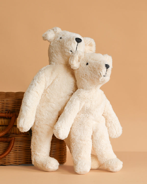 Two Senger Naturwelt Stuffed Animal - White Bears stand side by side, leaning against a wicker basket on a solid light brown background—a charming display of these sustainable plush toys.