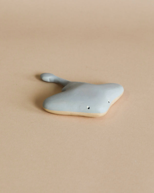 A handmade wooden stingray, colored in child-safe paint, placed on a beige surface. The stingray has a minimalist design with small, simple eyes.
