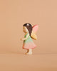 A Handmade Holzwald Maya Fairy, featuring brown hair adorned with a flower, a pastel green and pink dress, and yellow-pink wings, stands against a beige background. This enchanting piece comes with a postcard and is part of our collection of handmade wooden figures—perfect for imaginative play or whimsical decoration.