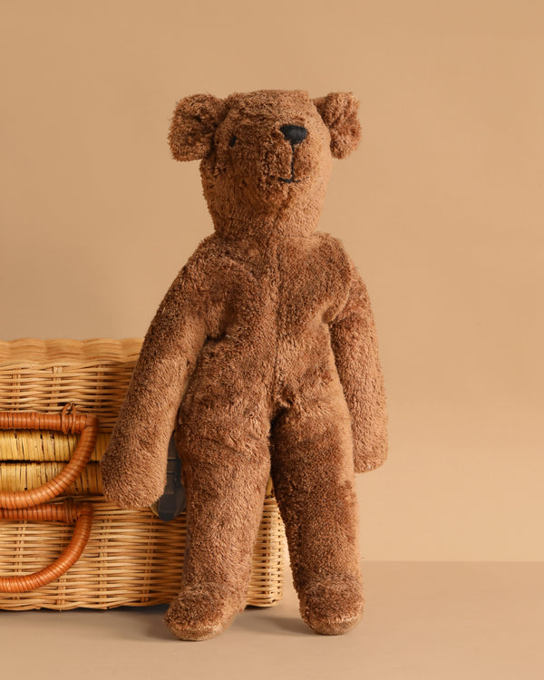 A large brown bear with a fuzzy, well-loved texture stands upright beside a wicker basket against a beige background—the Senger Naturwelt Stuffed Animal - Large Brown Bear, perfect for cozy playtime.
