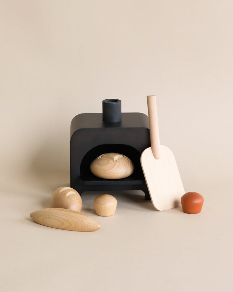 A minimalist composition featuring a small black cast iron oven, wooden kitchen utensils, a spatula, and various wooden oven accessories arranged neatly against a plain beige background.
Product Name: My Bakery