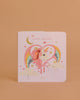 The Konges Sloejd Touch and Feel Book - Unicorn features a pastel pink cover with a unicorn, sparkly mane, rainbow, stars, clouds, and hearts on a peach background. This sensory cardboard book is perfect for young children to explore.