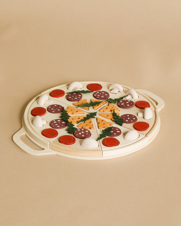 A Sabo Concept Wooden Pizza toy with colorful toppings including pepperoni, mushrooms, and green leaves on a round white tray, set against a beige background.