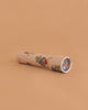 The Konges Sloejd Kaleidoscope - Cremona, featuring a floral pattern with berries, leaves, and colorful pearls, rests on a peach-colored surface with its viewing end angled slightly to the right.