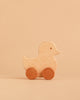 The Sabo Concept Rolling Duck - Natural, a wooden toy with round wheels crafted from natural materials, sits on a beige surface against a matching beige background.