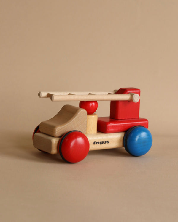 A colorful handcrafted Fagus Wooden Firetruck - Mini Series with red, blue, and natural wood hues, featuring a steering handle and smooth rolling wheels, displayed against a neutral background.