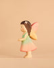 The Handmade Holzwald Maya Fairy and Postcard features a charming wooden fairy toy with yellow wings, a green and pink dress, and a flower in her brown hair, standing against a beige background. This delightful creation from Holzwald Toys beautifully captures the whimsical spirit of childhood imagination.