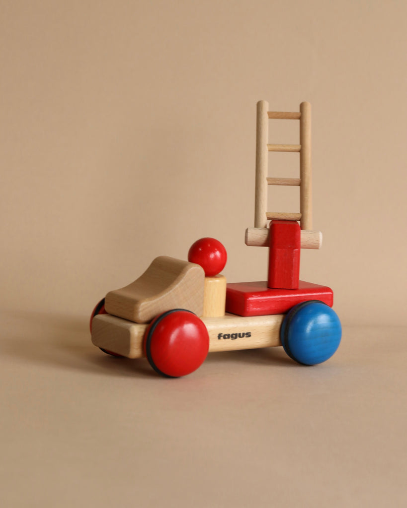 A handcrafted Fagus Wooden Firetruck - Mini Series with red and blue elements and a movable ladder, set against a plain beige background. The name "Fagus" is visible on the side.