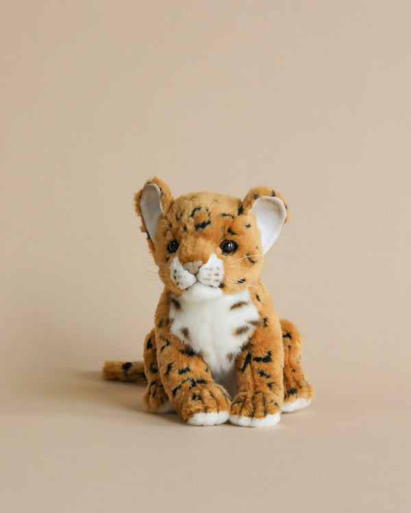 A sitting Jaguar Cub stuffed animal, artisan hand-sewn with realistic features, sits against a plain, light beige background. The jaguar cub has soft, stripe-patterned fur and an attentive expression.