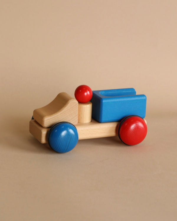A Fagus Wooden Truck - Mini Series with blue and red components, featuring rounded red wheels and blue rectangular blocks on a beige background.