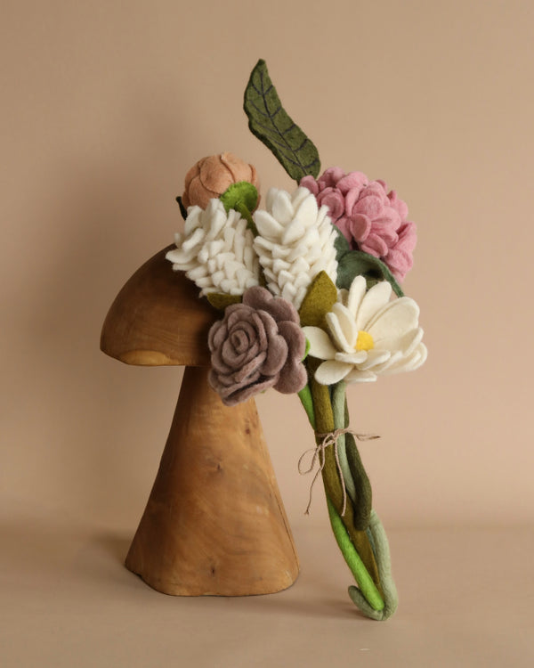A wooden mushroom sculpture adorned with a Felt Flower Bouquet - Daydream made from 100% natural New Zealand sheep's wool, tied neatly with a string, displayed against a neutral beige background.
