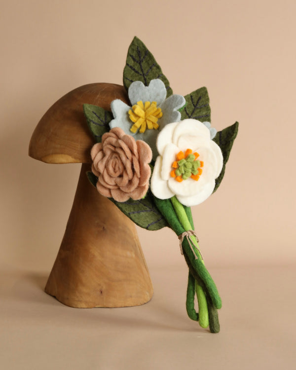 A wooden mushroom sculpture decorated with a bouquet of handmade Wildflower flowers from Nepal in shades of white, yellow, and dusty rose, set against a neutral background.