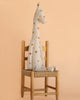 The Maileg Large Giraffe—a charming, soft, and polka-dotted plush safari friend—sits upright on a simple wooden chair against a peach-colored background.
