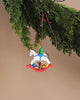 The Christian Ulbricht Ornament - Rocking Horse with Toys is a delightful festive piece showcasing a meticulously hand-painted toy horse accompanied by a teddy bear, blue ball, and yellow gift on a vibrant red swing. It elegantly hangs from a branch adorned with green foliage set against a simple background.