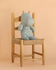 A Maileg Hippo, Medium - Blue Grey, sits on a woven wooden chair against a beige background, ready to join other Safari friends.