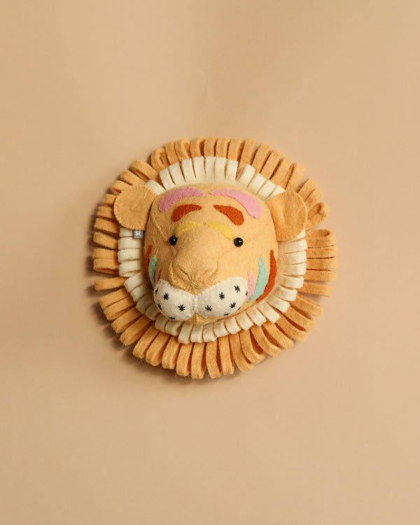 A colorful, plush tiger face with a vibrant mane made from organic wool, set on a warm beige background. The tiger features cute stitched details and a friendly expression.