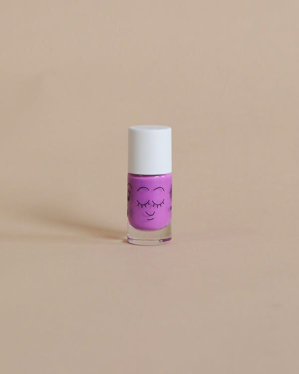 A small bottle of purple, cruelty-free Nailmatic nail polish with a cute, smiling face drawn on it, set against a plain beige background.