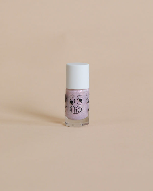 A small bottle of pink, vegan cruelty-free Nailmatic Elliot glitter nail polish with a cartoon face drawn on it, standing against a plain beige background.