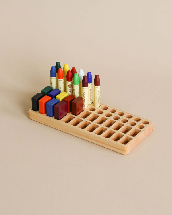 A Crayon Tray For Stockmar -24 x 24 Slots, crafted from Linden wood, holds a variety of colorful Stockmar sticks and blocks, organized neatly against a plain beige background.