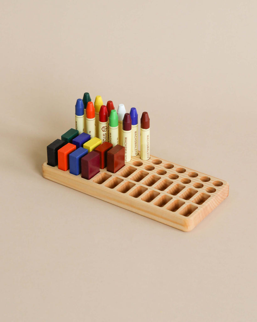 A Crayon Tray For Stockmar -24 x 24 Slots, crafted from Linden wood, holds a variety of colorful Stockmar sticks and blocks, organized neatly against a plain beige background.