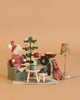 The Maileg Cozy Christmas Set features a winter ski mouse in a red sweater by a mini fireplace, with a tiny Christmas tree, coffee table, mugs, book, and a vintage floor lamp, all on a warm beige background.