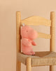 A Maileg Hippo, Small - Rose, made from soft fabric sits upright on a wooden chair with a woven seat, against a beige background.