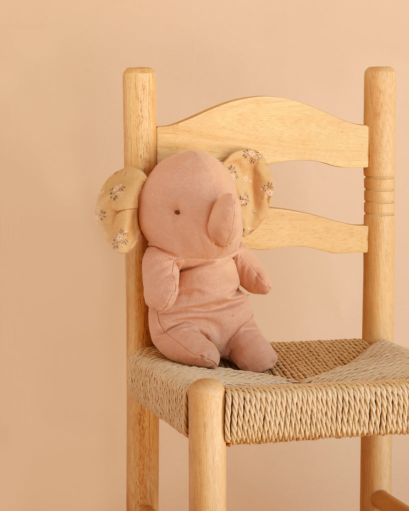 The Maileg Elephant, Small - Powder is a soft, light brown plush toy crafted from the gentlest fabric and features charming patterned ears. Seated on a woven wooden chair against a beige backdrop, it’s an adorable addition to any collection of Safari friends.