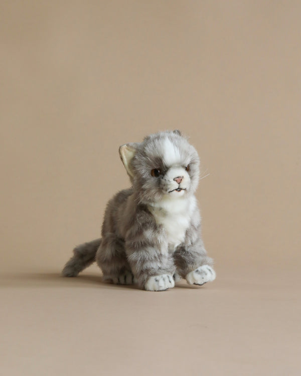 A Grey Cat Stuffed Animal with fluffy gray and white fur, sitting upright against a light beige background. The cat has bright, expressive eyes and a small open mouth, hand-sewn to capture lifel