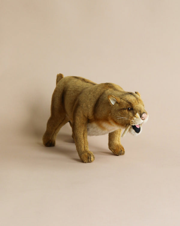 A realistic plush toy of a Saber Tooth Tiger captured mid-stride against a plain beige background. This artisan plush animal shows detailed features such as fierce eyes and visible teeth.