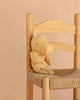 The Maileg Hippo, Small - Cream Yellow from the Safari friends collection, crafted from soft fabric, sits on a woven straw chair with a light wooden frame against a plain beige background.
