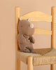 The Maileg Rhino, Small - Chocolate, crafted from soft fabric in a rich brown hue, sits on a woven wooden chair against a beige background—ready to join your collection of Safari friends.
