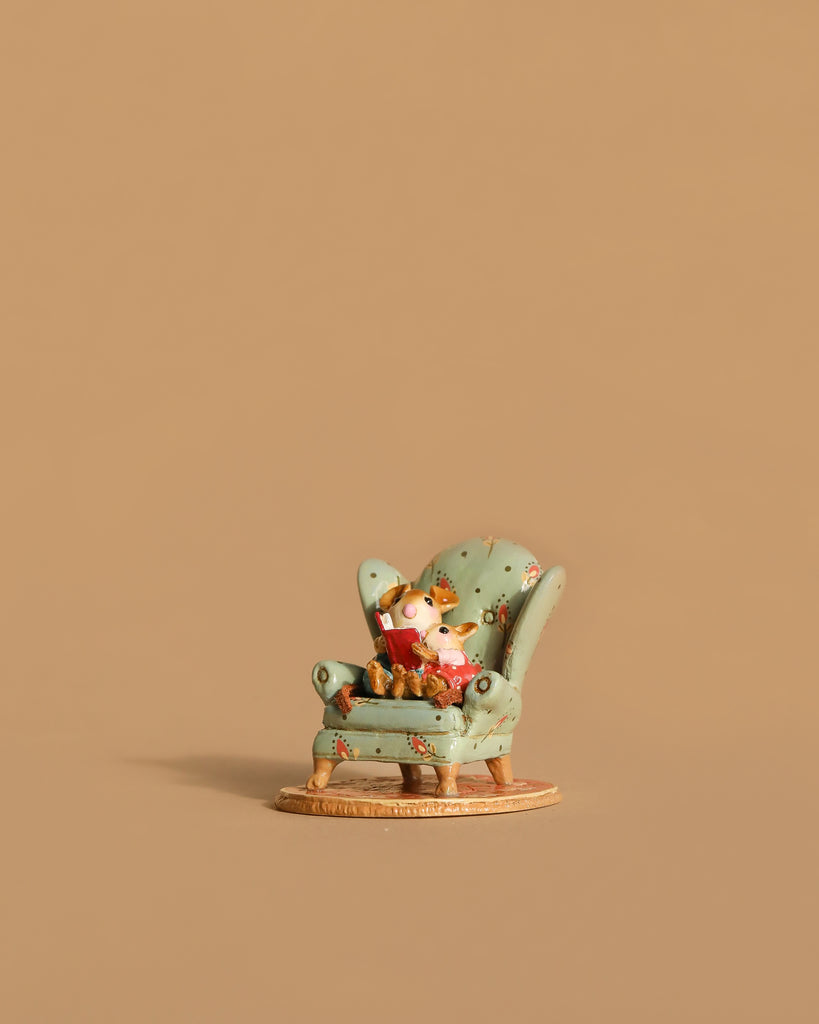 The Wee Forest Folk Tiny Collectible - Sharing A Story (Not a Toy) features a miniature fox figurine seated in a green floral armchair, displayed on a tan surface with a plain tan background.