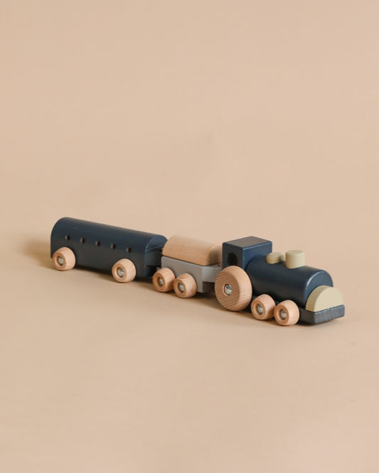Sentence with Product Name: A Mini Wooden Train crafted from responsibly sourced beech wood, with blue and natural wood colors, is displayed against a light beige background. The train includes a locomotive and two attached cars with round wheels.
