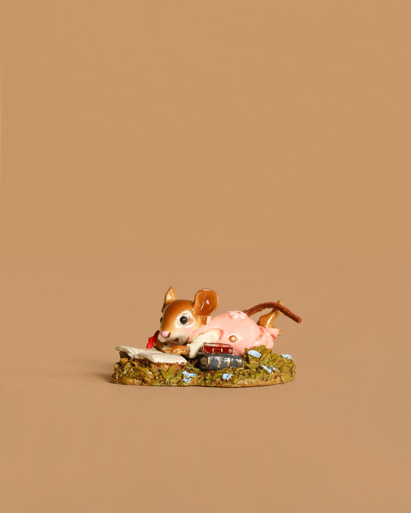 The Wee Forest Folk Tiny Collectible - Meadow Musing features a small handmade mouse in a pink dress lying on its stomach, reading a book on a grassy base.