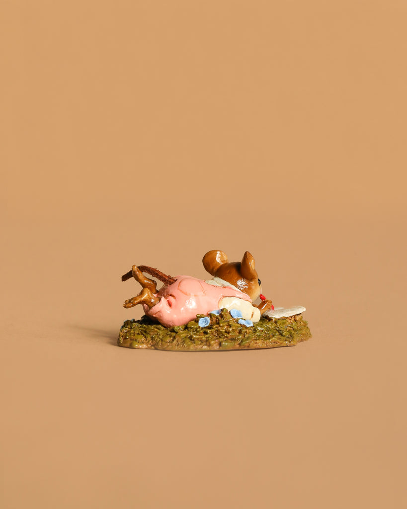 The Wee Forest Folk Tiny Collectible - Meadow Musing (Not a Toy) features a hand-sculpted brown squirrel lying beside a pink object on a textured green base with blue flowers, set against a plain beige background.