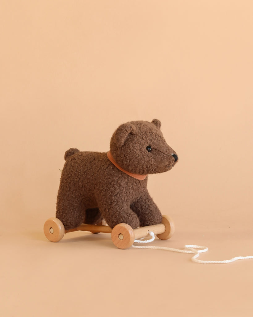 Pull-Along Raoul is a plush brown bear toy on wooden wheels, featuring a string for easy pulling and set against a beige background—perfect for encouraging gross motor skills during playtime.