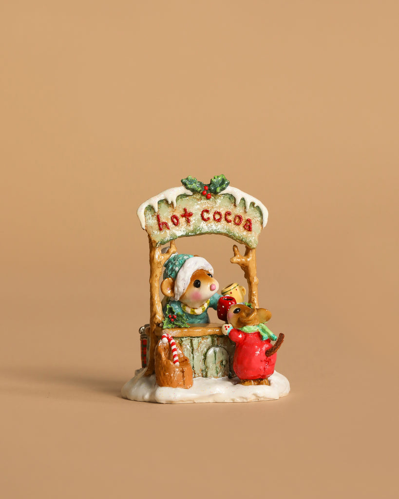 The Wee Forest Folk Tiny Collectible - Hot Cocoa Comin' Up! features a hand-sculpted mouse in a green hat at a hot cocoa stand, serving a cup to a reindeer in red scarf, with holly and snow accents on a beige background.