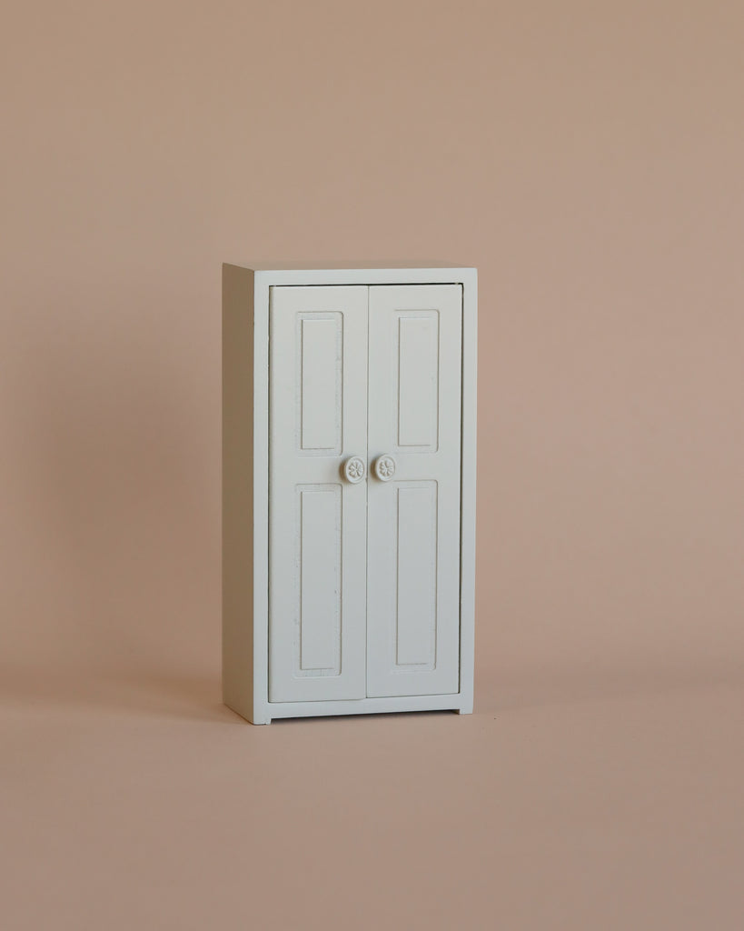 A small white cabinet with two doors and round knobs stands against a plain beige background, making it a perfect addition to your Maileg Bedroom Set for storing Maileg mouse accessories or complementing other Maileg mouse furniture.