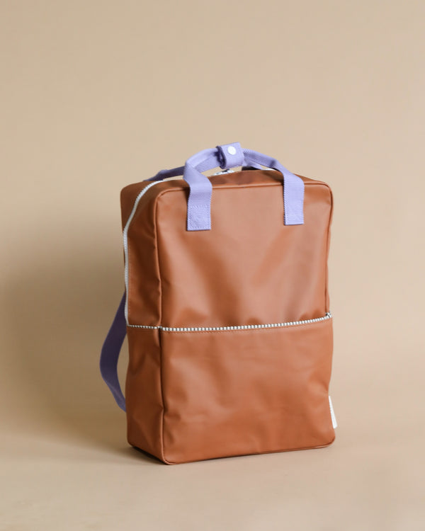 A stylish Sticky Lemon Backpack | Uni | Buddy Brown with purple straps and a visible front YKK zipper pocket stands against a plain beige background.