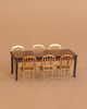The Maileg Dining Room Set features a miniature dark brown long dining table with six gold mouse-size chairs, all arranged against a plain beige background.