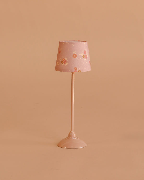 The Maileg Floor Lamp, Miniature - Dark Powder features a small pink stand and floral-patterned lampshade, making it perfect for dollhouse decor. Displayed against a simple beige background.