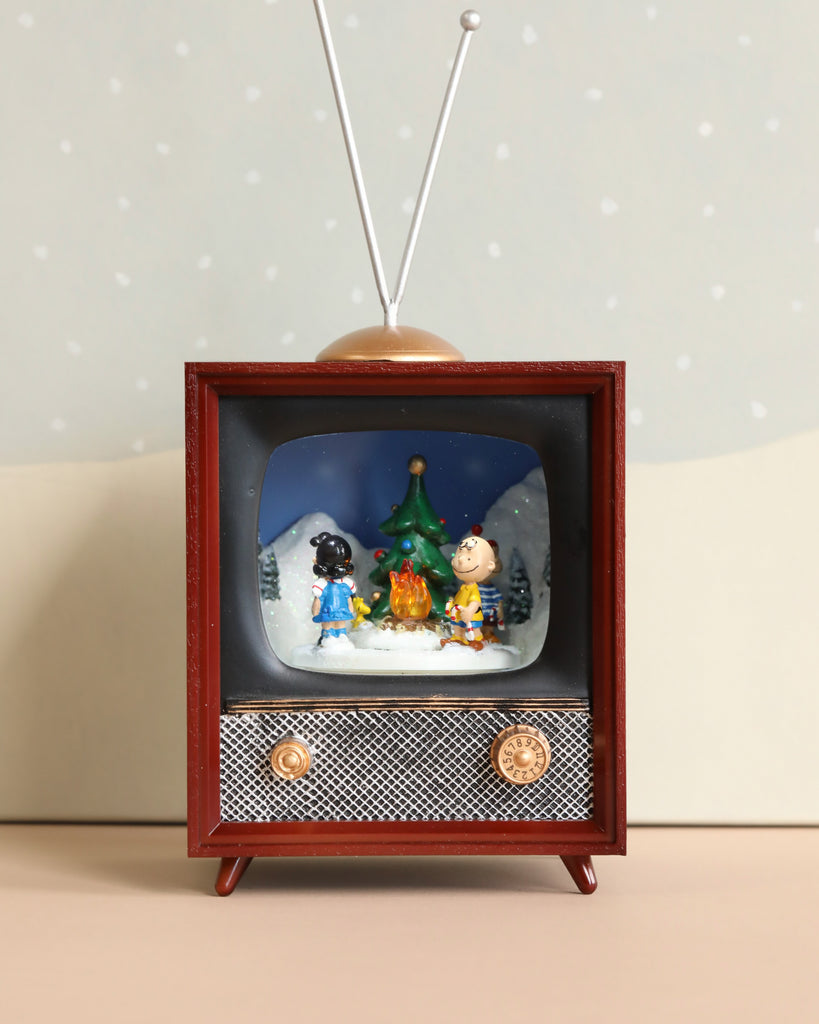 Introducing the Charlie Brown Christmas Music TV: This charming miniature vintage television set features a brown frame and antennas. It lights up to showcase a 3D scene with two beloved cartoon characters by a Christmas tree, while gentle snow falls around them. A small campfire flickers in front, accompanied by a soft, festive Christmas melody playing in the background.