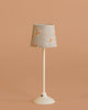 The Maileg Floor lamp, Miniature - Sand features a slender white stem and a floral-patterned shade, displayed against a plain beige background.