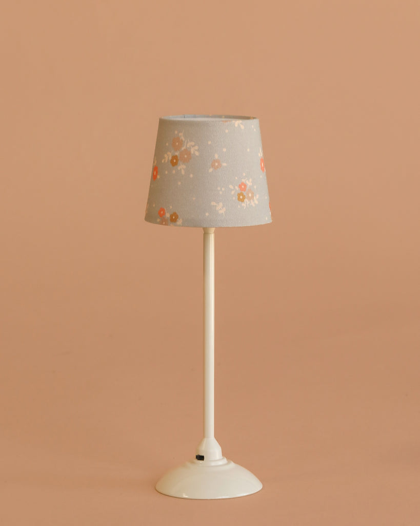 The Maileg Floor lamp, Miniature - Sand features a slender white stem and a floral-patterned shade, displayed against a plain beige background.