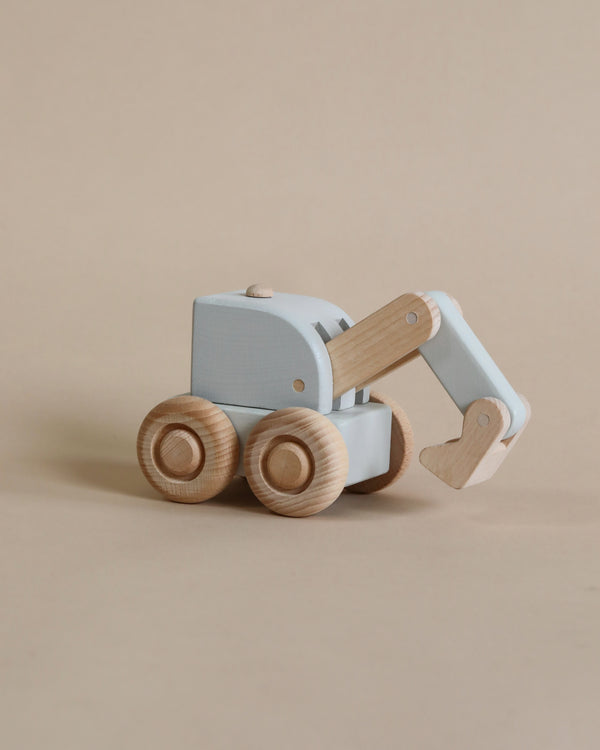 The Wooden Digger is a small, light blue vehicle crafted from responsibly sourced beech wood. It features a movable arm, four round wheels, and is painted with non-toxic paint on a beige background, showcasing a simple and minimalist design.